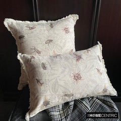 Two decorative pillows with a beige fabric featuring insect patterns, placed on a soft fabric with a checkered design underneath them.