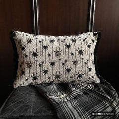 Halloween lumbar pillow cover with spider design on a woven jacquard fabric and beads and lace embroidery, set against a dark wood background with a plaid blanket.