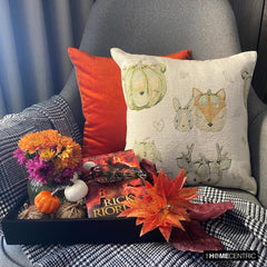 Fall Halloween home decor pillow cover, A woven jacquard throw pillow cover with pumpkin fox design and subtle fall colors for Autumn Decor set on a grey chair with a black throw and layered with an orange velvet pillow cover. Decorated with a tray containing maple leaves, pumpkin, book, and fall colored flowers, creating a perfect, cozy, and comfortable fall decor setting. Handcrafted pillow cover from The HomeCentric's Fall Collection.