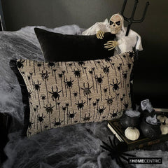 Halloween pillow with black spider silver beads embroidery, skeleton figure, and Halloween-themed decor including small pumpkins, witch pot with white smoke, spiders and books.