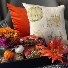 Fall Halloween home decor pillow cover, A woven jacquard throw pillow cover with pumpkin fox design and subtle fall colors for Autumn Decor set on a grey chair with a black throw and layered with an orange velvet pillow cover. Decorated with a tray containing maple leaves, pumpkin, book, and fall colored flowers, creating a perfect, cozy, and comfortable fall decor setting. Handcrafted pillow cover from The HomeCentric's Fall Collection.
