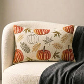 Orange, beige & ivory color pumpkin pattern with maple leaves lumbar pillow cover crafted on a woven jacquard fabric for fall & Halloween decor from The HomeCentric's autumn decor collection. The oblong cushion cover is set on a black stool covered with a houndstooth pattern throw, paired ith maple leaves and white, orange, & burlap pumpkins, to create a cozy fall season vibe, in a natural setting with orange-red leaves in the background. Explore more of The HomeCentrc's Autumn Decor.