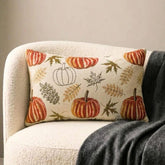 Orange, beige & ivory color pumpkin pattern with maple leaves lumbar pillow cover crafted on a woven jacquard fabric for fall & Halloween decor from The HomeCentric's autumn decor collection. The oblong cushion cover is set on a black stool covered with a houndstooth pattern throw, paired ith maple leaves and white, orange, & burlap pumpkins, to create a cozy fall season vibe, in a natural setting with orange-red leaves in the background. Explore more of The HomeCentrc's Autumn Decor.