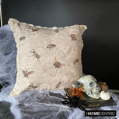 Close-up of a decorative pillow with a vintage insect design featuring bees, beetles, and flies, styled in a spooky Halloween setting with a skull and spider decorations.