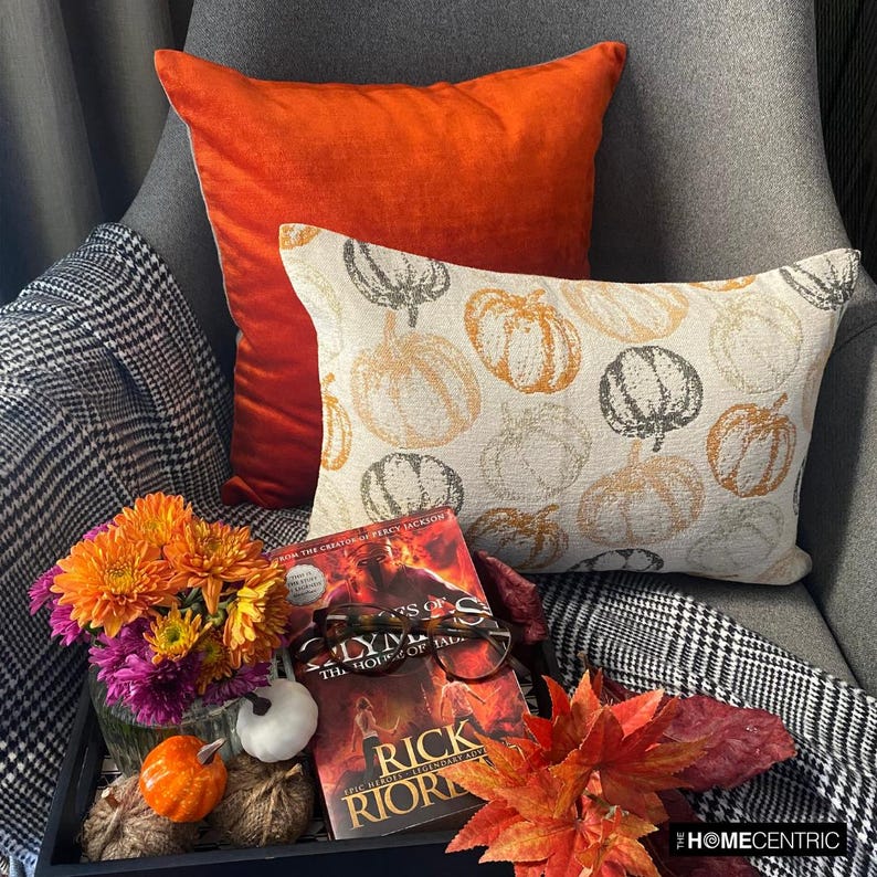Orange woven jacquard pumpkin pattern lumbar pillow cover for Halloween & Fall home decor. Ideal for modern or country style home decor, the oblong cushion cover is set on a grey chair paired with a solid orange velvet throw pillow cover from The HomeCentric. A tray is place with the pillows on chair with maple leaves, burlap pumpkins and flower arrangement in fall hues. The look is finished with a black and white monochrome checkered throw. Explore more of fall & Halloween Collection by The HomeCentric!