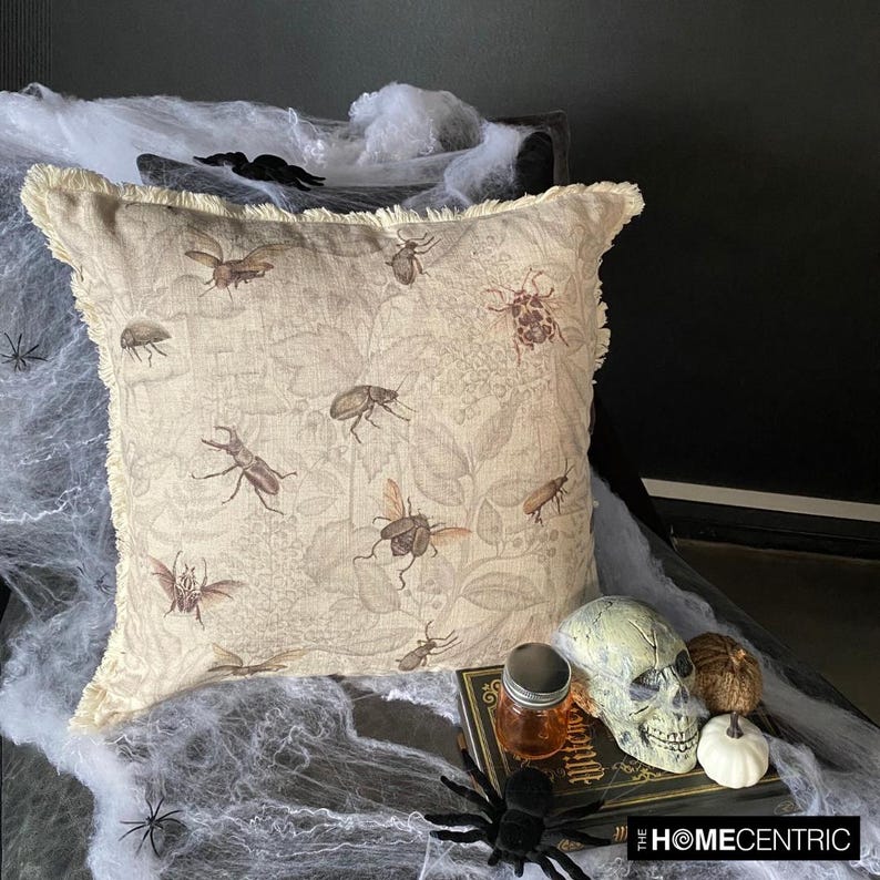 Decorative pillow with a vintage insect design, including flies, beetles, and bees, placed beside a skull, jar, and pumpkin for a spooky Halloween setting.