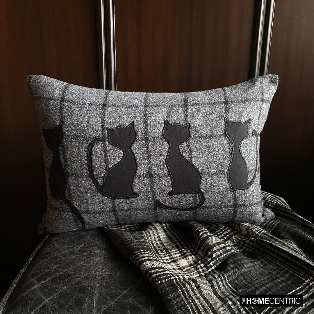 Close-up of a black cat-themed decorative pillow on wool plaid fabric, ideal for Halloween or fall decor.