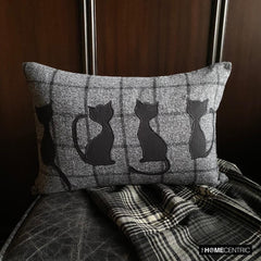 Close-up of a black cat-themed decorative pillow on wool plaid fabric, ideal for Halloween or fall decor.