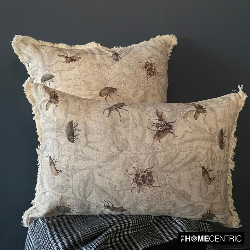 Two decorative pillows with a vintage insect design featuring beetles and bees, stacked on a checkered blanket with frayed edges.