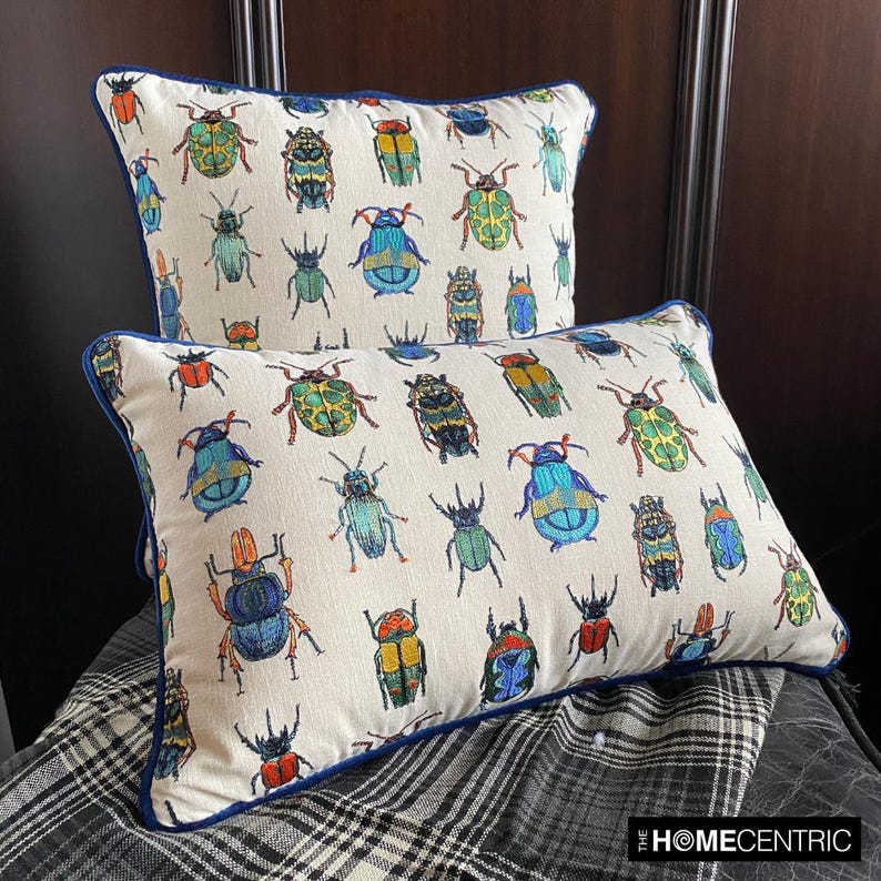 Two beetle-themed pillow cover with navy trim, placed on a checkered blanket with a dark background.