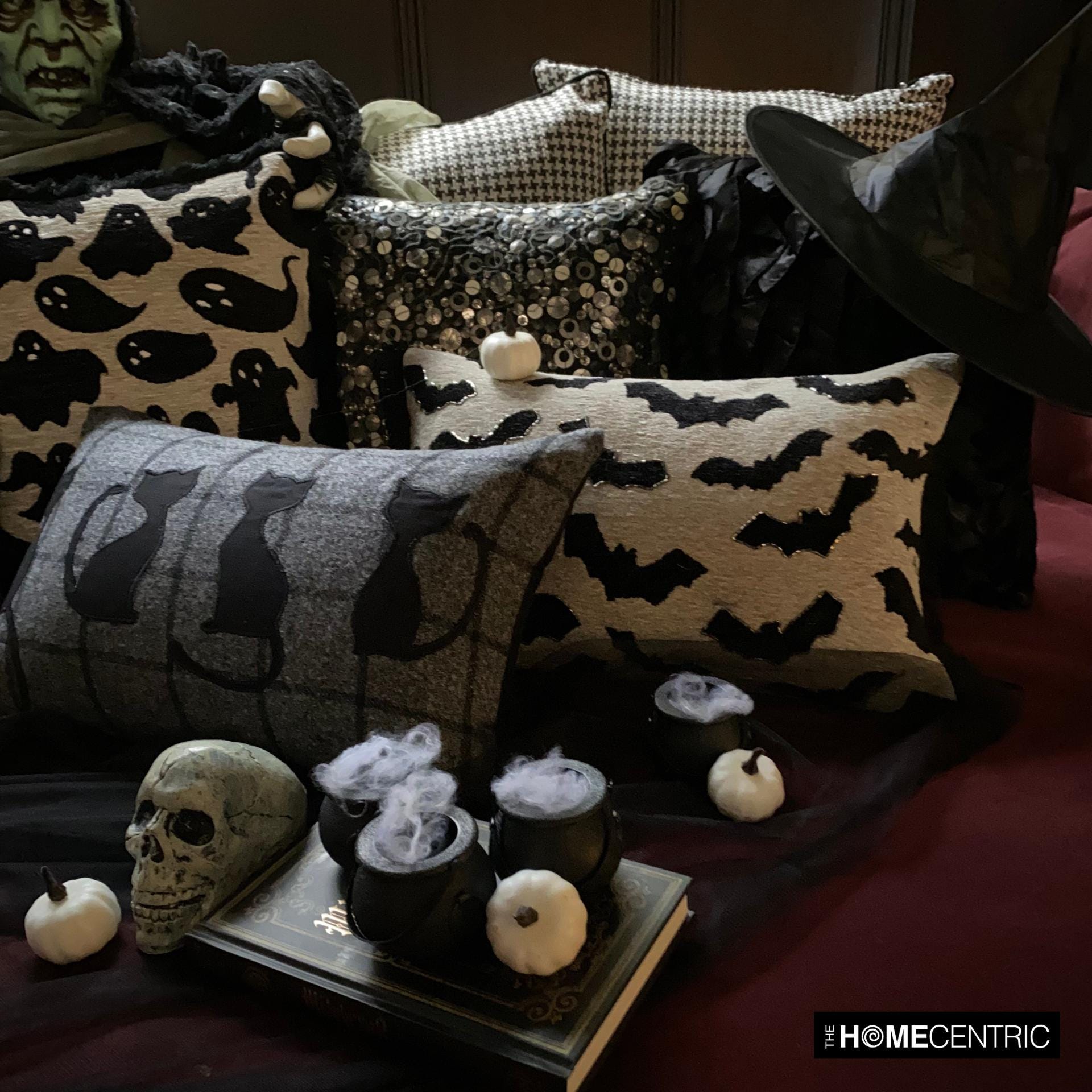 Spooky Halloween decor with multiple Halloween-themed pillows, including black cat, ghost, and bat designs, along with skeleton and potion bottle props.