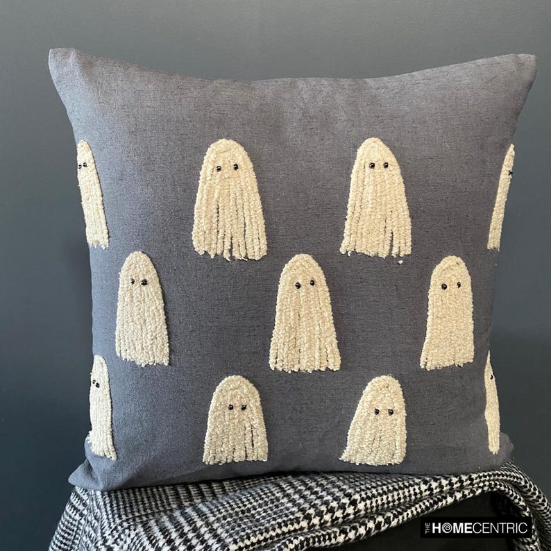 Decorative Halloween grey embroidered ghost throw pillow cover placed on a black stool covered with a black & white monochrome throw. 