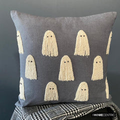 Decorative Halloween grey embroidered ghost throw pillow cover placed on a black stool covered with a black & white monochrome throw. 