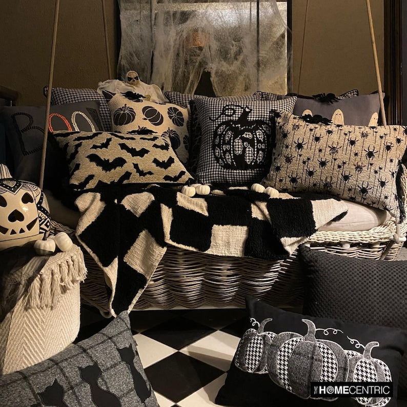 Spooky Halloween decorative pillow covers surrounded by festive Halloween decorations like pumpkins and spider web on a swing decorated with black & white checkered throw. 