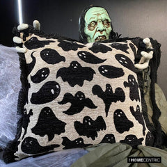 Halloween decorative throw pillow cover with black ghost pattern and fringed edges, a scary Halloween ghost holding the pillow cover on a chair wrapped with spider web for Halloween home decor. 