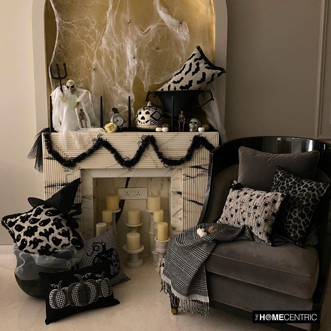 Halloween fireplace corner decorated with various spooky themed pillow covers including ghost, bats, spiders and pumpkin designs. Decorated with Halloween fireplace decor with witch pot and a witch hat, with scary Halloween ghost, black candles and tiny skulls and pumpkins. 