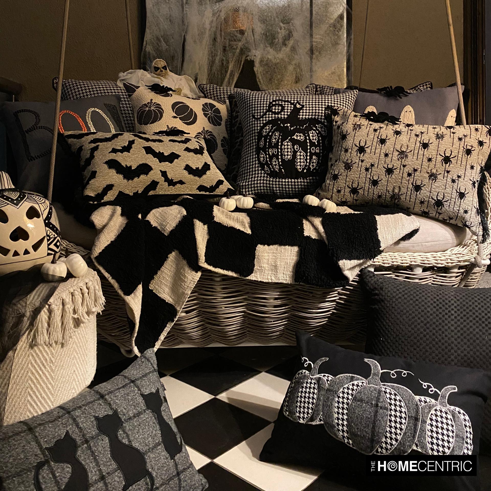 Cozy Halloween-themed sofa with multiple decorative pillow covers designed around the Halloween decor theme  including bats, spiders, witch cats and pumpkin patterns in a spooky Halloween setup with spider web and pumpkins.
