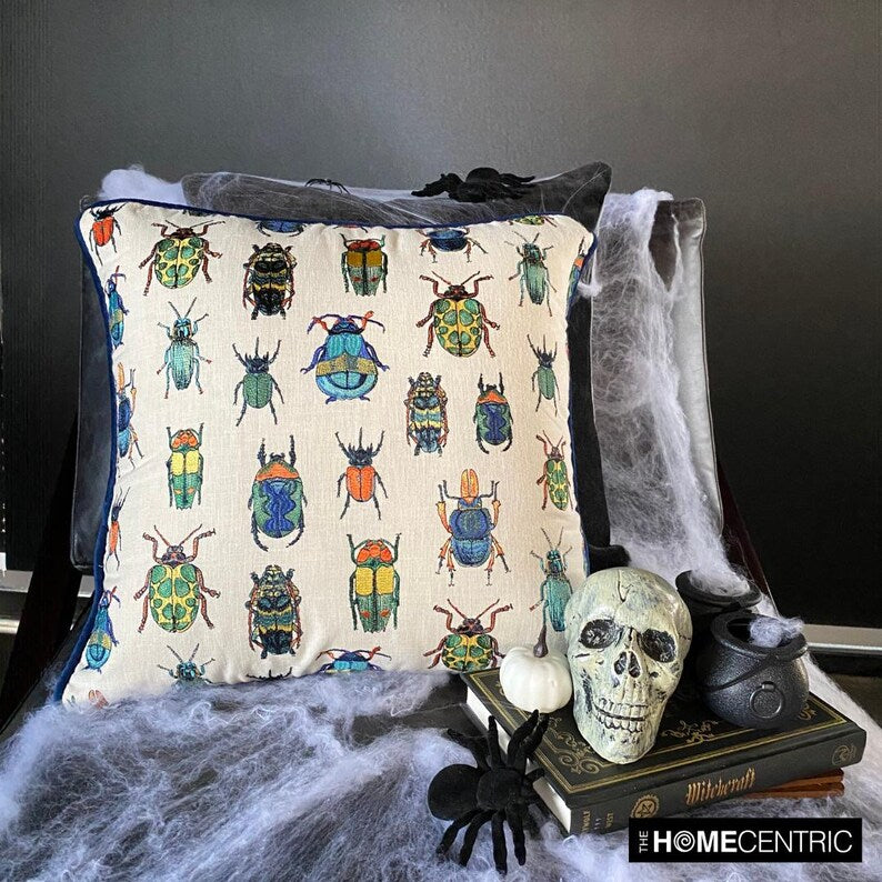 Beetle-patterned embroidered pillow cover placed on a black chair with Halloween decorations like a skull, pumpkin, and spider webs.
