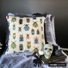 Beetle-patterned embroidered pillow cover placed on a black chair with Halloween decorations like a skull, pumpkin, and spider webs.