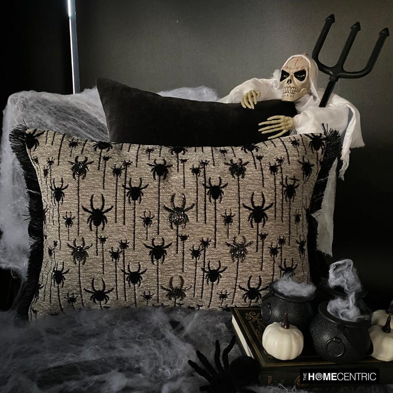 Halloween pillow with black spider embroidery surrounded by spooky decor, including a skeleton figure and foggy cauldrons.