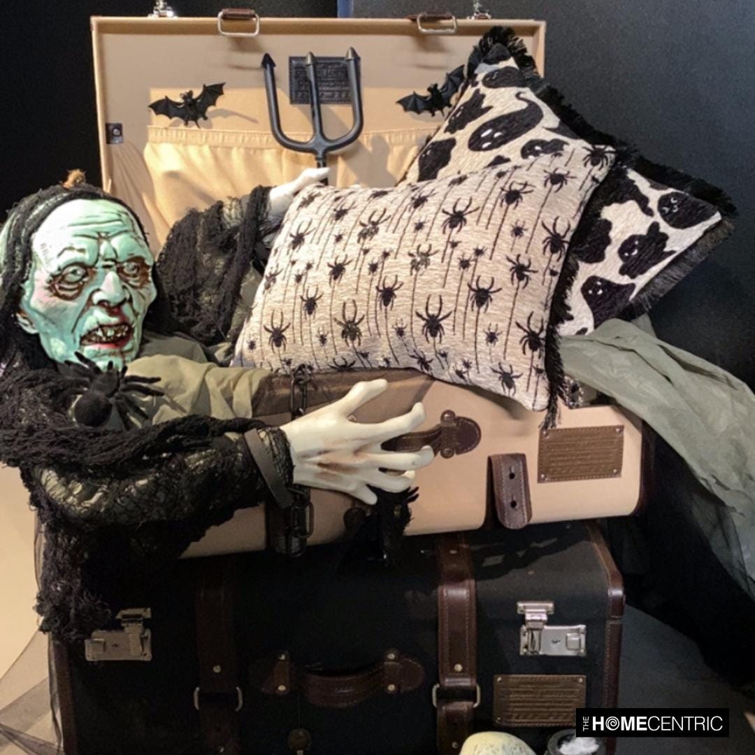 Halloween trunk setup with ghost print throw pillow cover and a decorative beaded spider lumbar pillow cover, held by a scary skeleton or ghost sitting in a travel trunk with bats and spiders coming out of the trunks. 