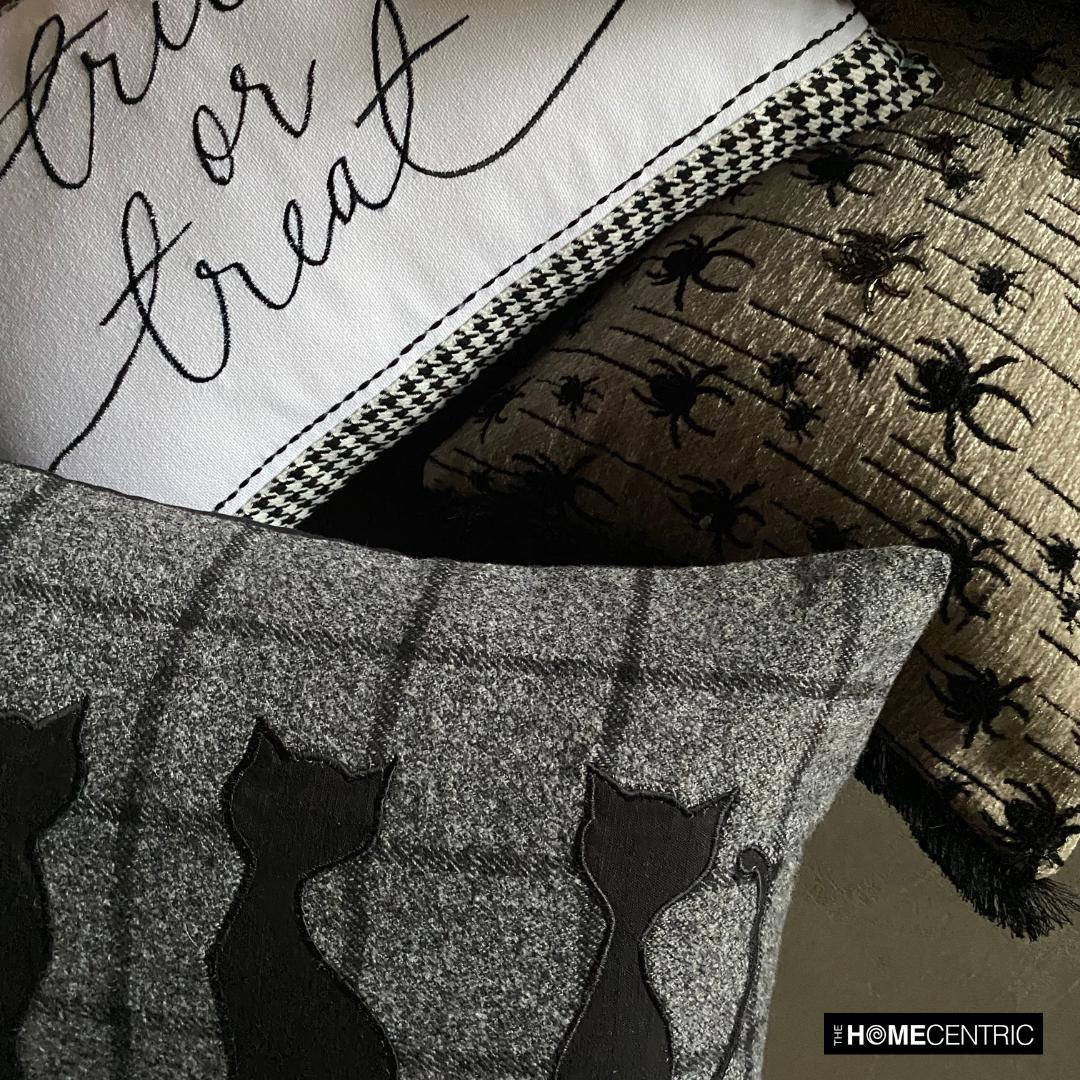 Halloween pillows stacked together, including a black cat design pillow, with a 'trick or treat' pillow and a spider-themed pillow