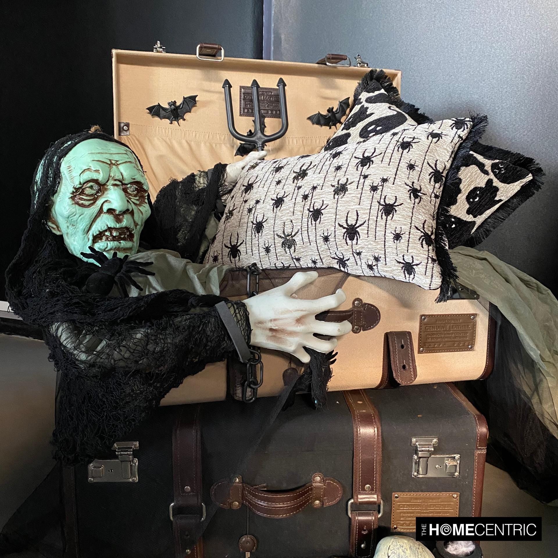 Creepy Halloween display with woven spider-patterned lumbar pillow cover and a haunted figure in a suitcase holding the pillow covers to create a spooky Halloween look. 