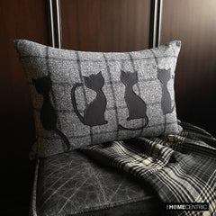 Close-up of a black cat-themed decorative pillow on wool plaid fabric, ideal for Halloween or fall decor, on a black & white plaid throw against a wooden background.