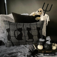 Halloween home decor featuring spooky black cat lumbar pillow cover with plaid design on a wool fabric, skeleton prop, spider webs, and eerie decorations creating a haunting Halloween vibe!