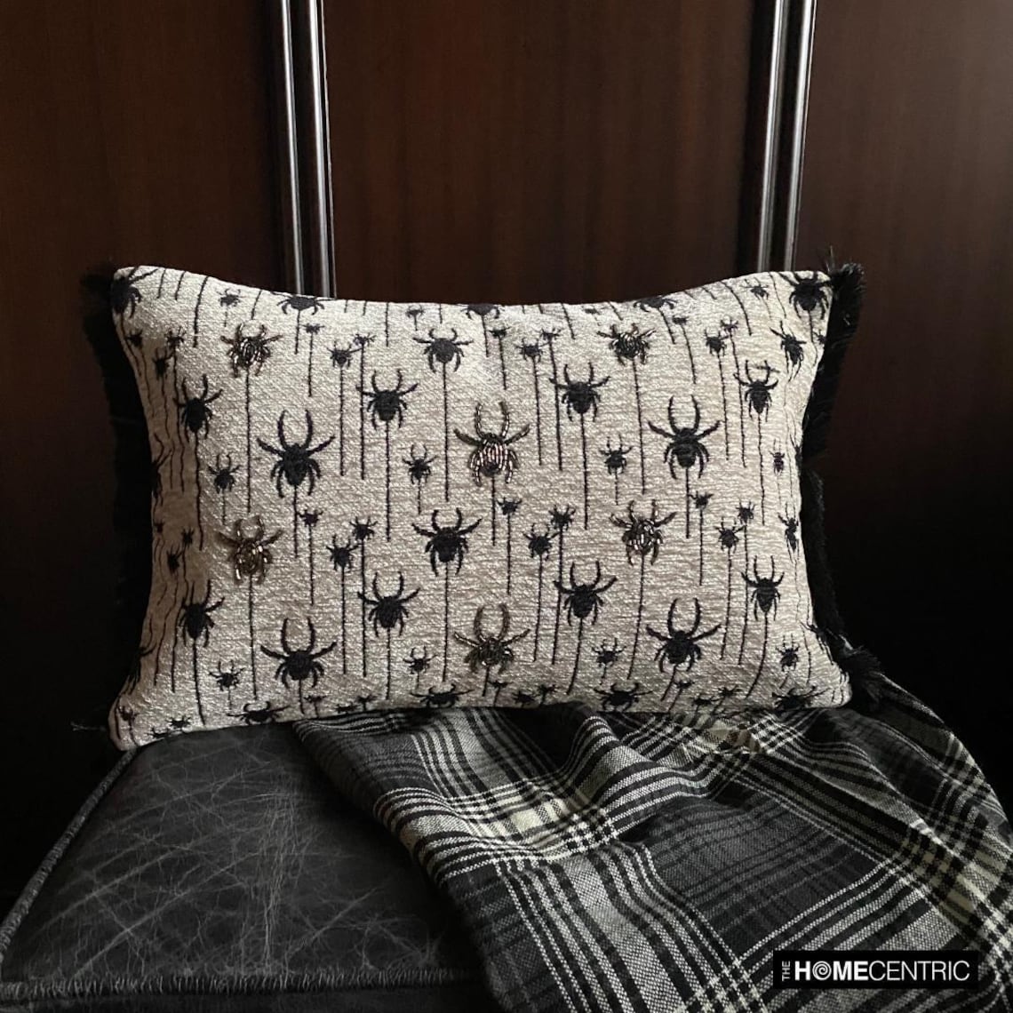 Halloween lumbar pillow cover with spider design on a woven jacquard fabric and beads and lace embroidery, set against a dark wood background with a plaid blanket.