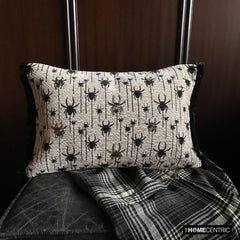 Halloween lumbar pillow cover with spider design on a woven jacquard fabric and beads and lace embroidery, set against a dark wood background with a plaid blanket.