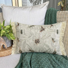 A pillow with a floral insect design on a beige fabric, surrounded by Halloween-themed decorations such as a skull, books, and a pumpkin, set against a webbed backdrop.