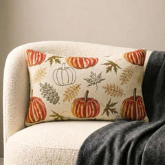 Orange, beige & ivory color pumpkin pattern with maple leaves lumbar pillow cover crafted on a woven jacquard fabric for fall & Halloween decor from The HomeCentric's autumn decor collection. The oblong cushion cover is set on a black stool covered with a houndstooth pattern throw, paired ith maple leaves and white, orange, & burlap pumpkins, to create a cozy fall season vibe, in a natural setting with orange-red leaves in the background. Explore more of The HomeCentrc's Autumn Decor.