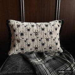 Halloween lumbar pillow cover with spider design on a woven jacquard fabric and beads and lace embroidery, set against a dark wood background with a plaid blanket.