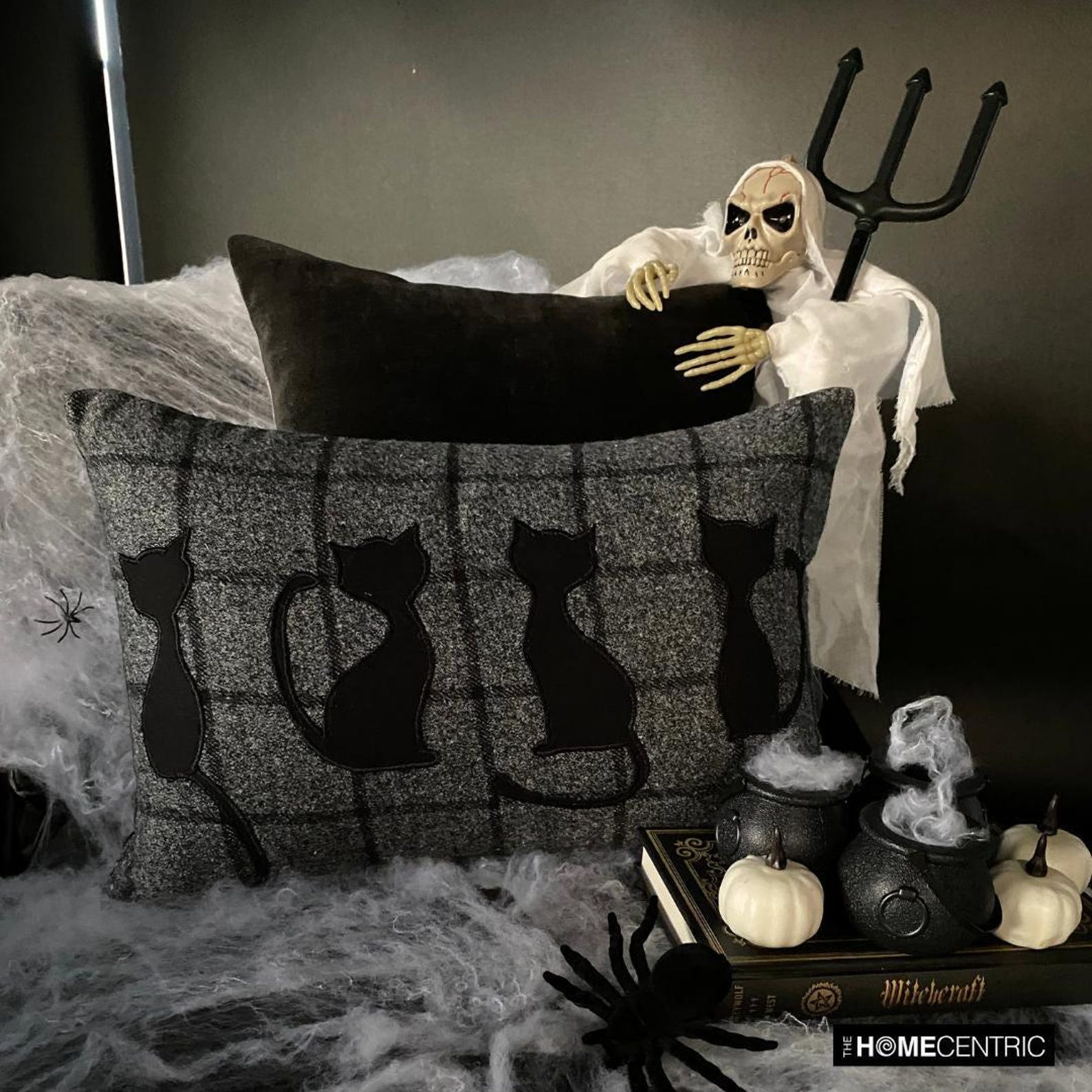 Close-up of a black cat-themed decorative pillow on wool plaid fabric, ideal for Halloween or fall decor.