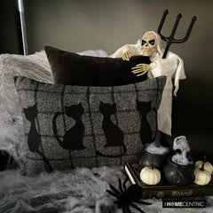 Close-up of a black cat-themed decorative pillow on wool plaid fabric, ideal for Halloween or fall decor.
