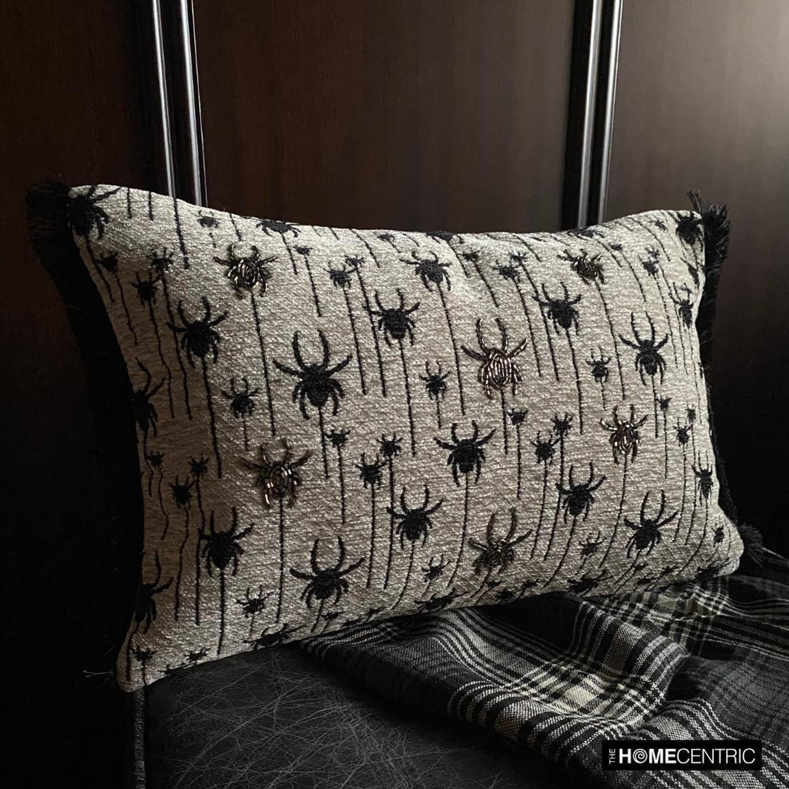 Halloween pillow with black spider silver beads embroidery, skeleton figure, and Halloween-themed decor including small pumpkins, witch pot with white smoke, spiders and books.