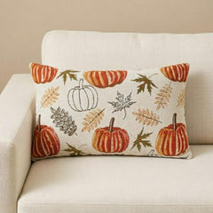 Orange, beige & ivory color pumpkin pattern with maple leaves lumbar pillow cover crafted on a woven jacquard fabric for fall & Halloween decor from The HomeCentric's autumn decor collection. The oblong cushion cover is set on a grey chair covered with a black & white checks throw, and layered with an orange solid velvet throw pillow cover. A finishing touch is added with a tray containing maple leaves, book, burlap pumpkins and flowers in orange and purple color in a vase. 