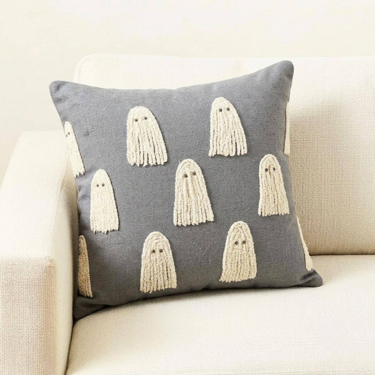 Skeleton holding a grey spooky ghost pillow cover surrounded by Halloween decor such as a skull and a witch pot placed on a book.