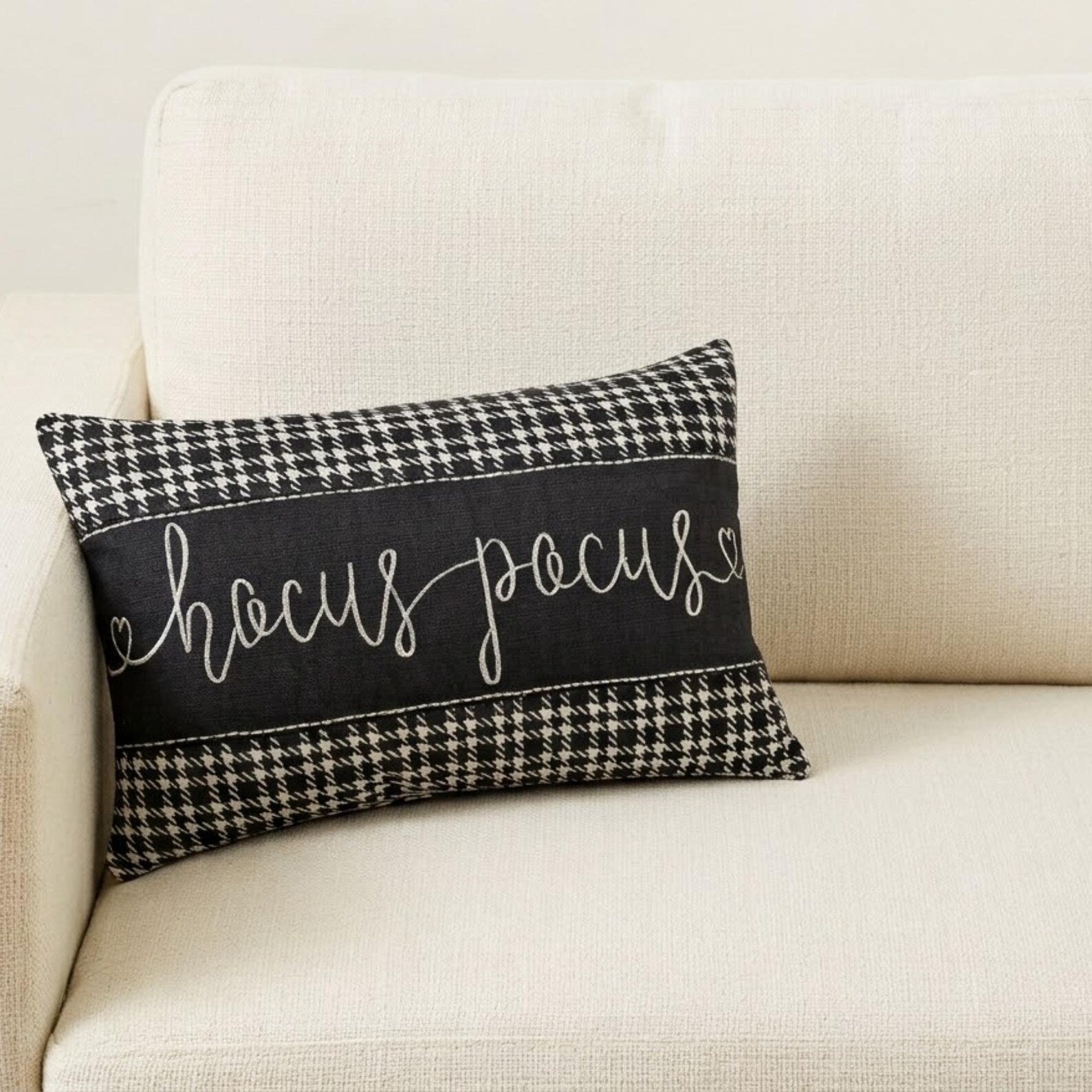 Close-up shot of a 'Hocus Pocus' black and white cotton houndstooth rectangle pillow cover on a couch with a gray throw.