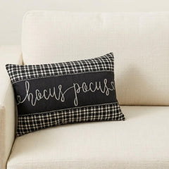 Close-up shot of a 'Hocus Pocus' black and white cotton houndstooth rectangle pillow cover on a couch with a gray throw.